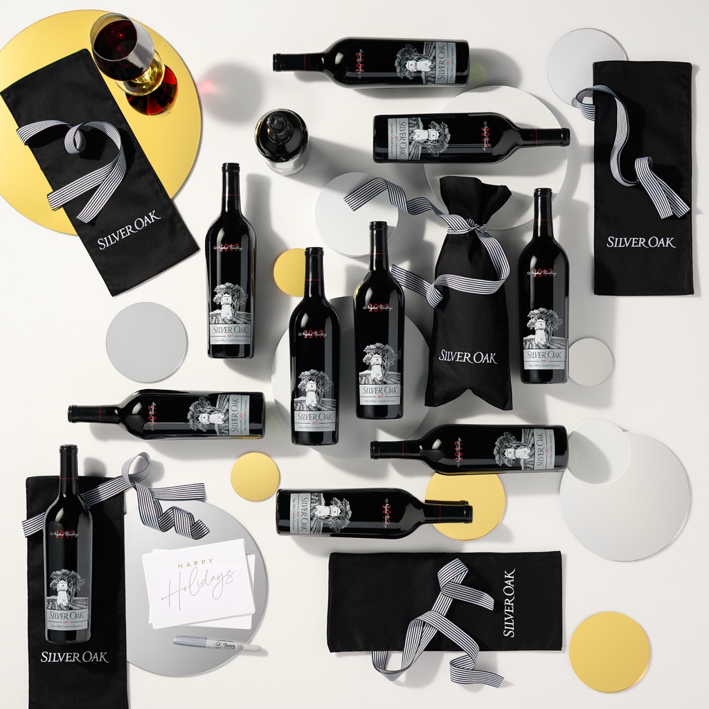 Overhead flatlay of Silver Oak cabernet bottles, gift bags, ribbon and holiday cards on a white tabletop