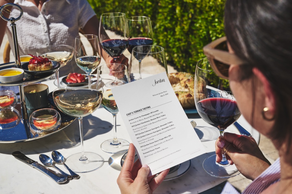 Guest reading a chef's terrace tasting menu over a table of wine pairings at Jordan Winery in Alexander Valley