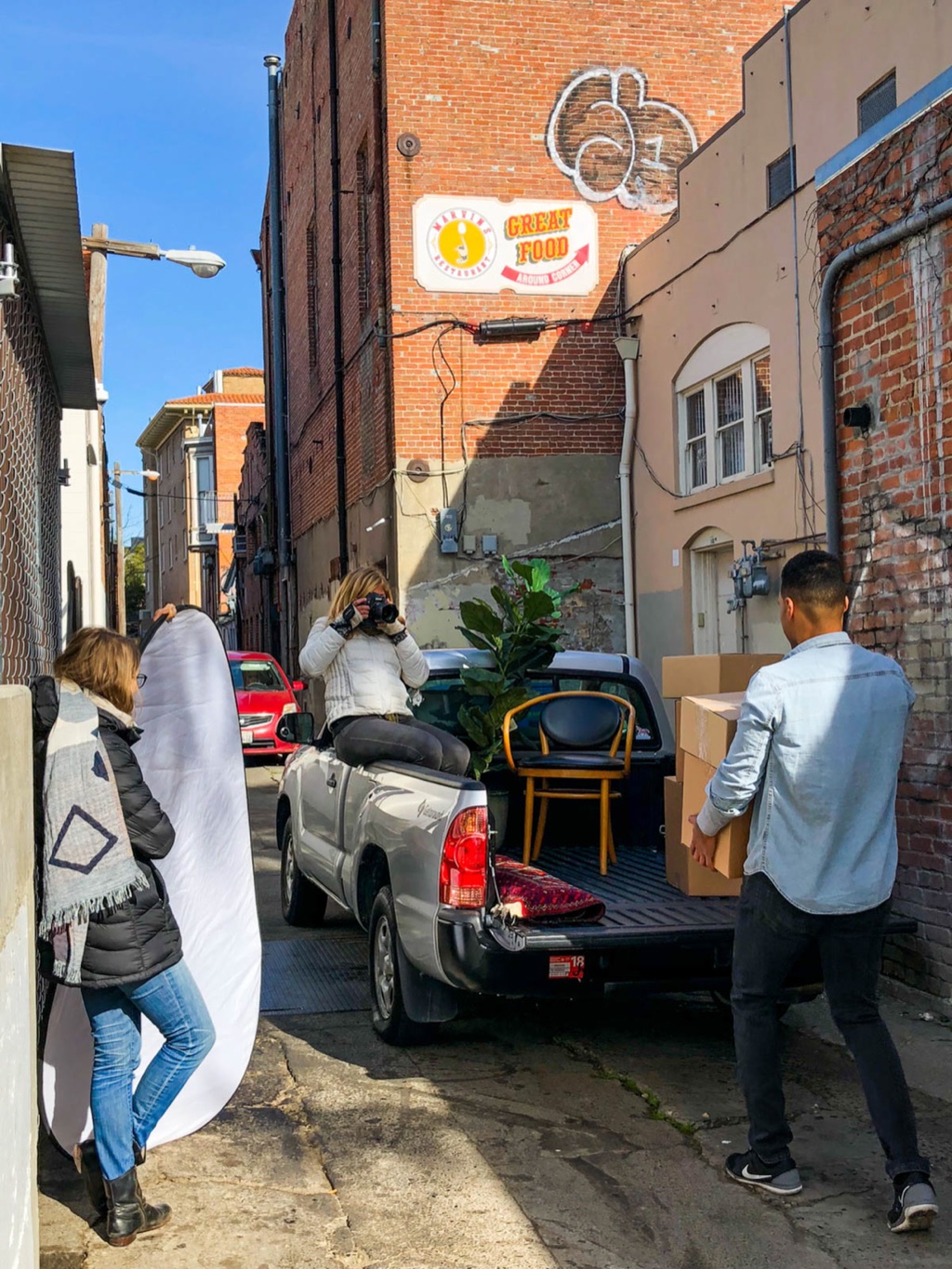Shooting furniture staged in a pickup bed in a brick alley, assistant holding a bounce
