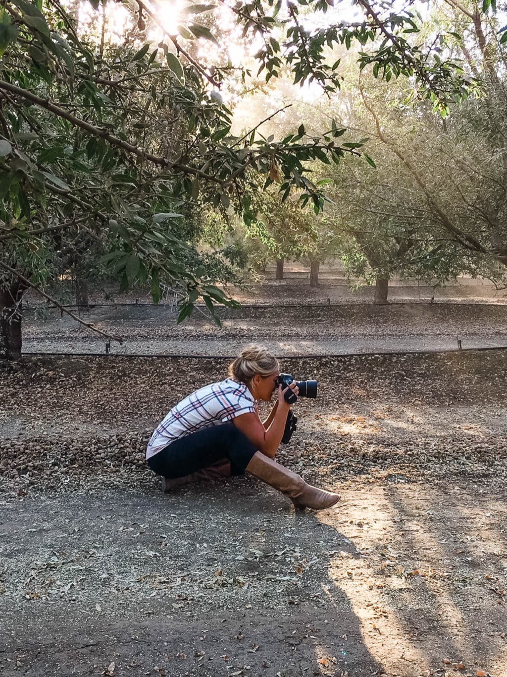 Dawn Heumann crouched in an almond orchard shooting through low morning light