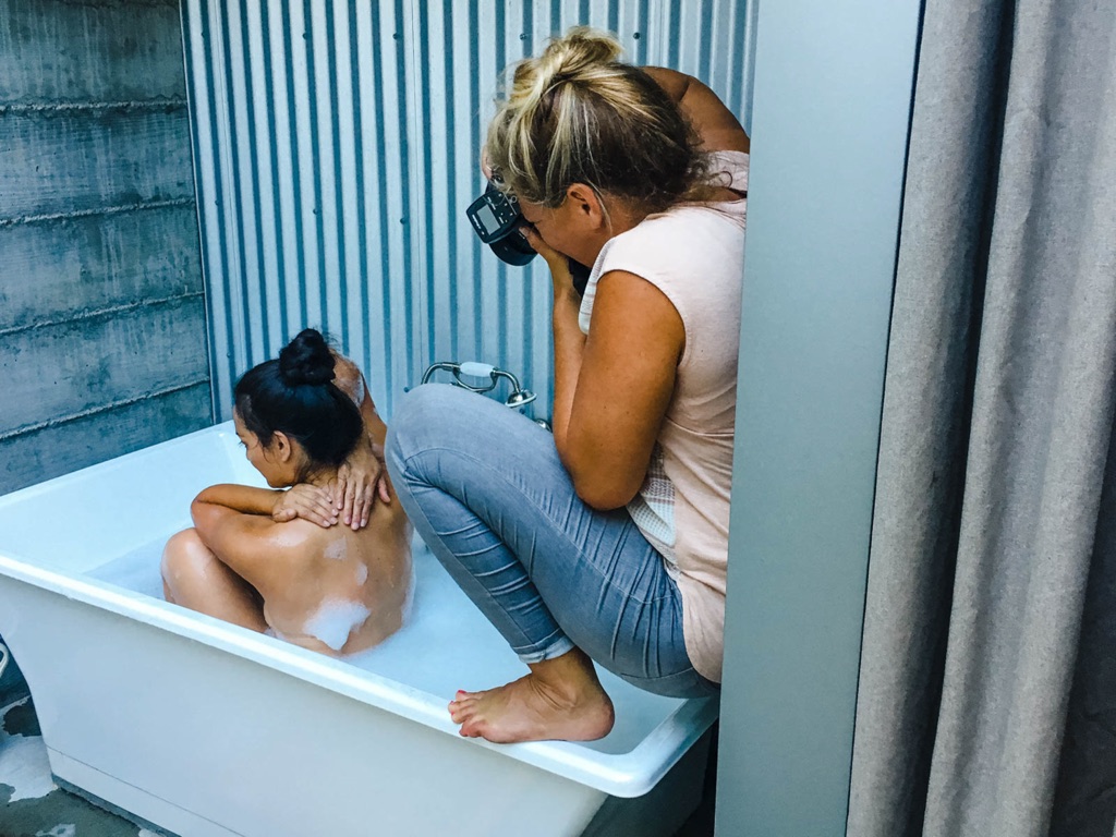 Dawn Heumann perched on the edge of a freestanding tub photographing a bath scene