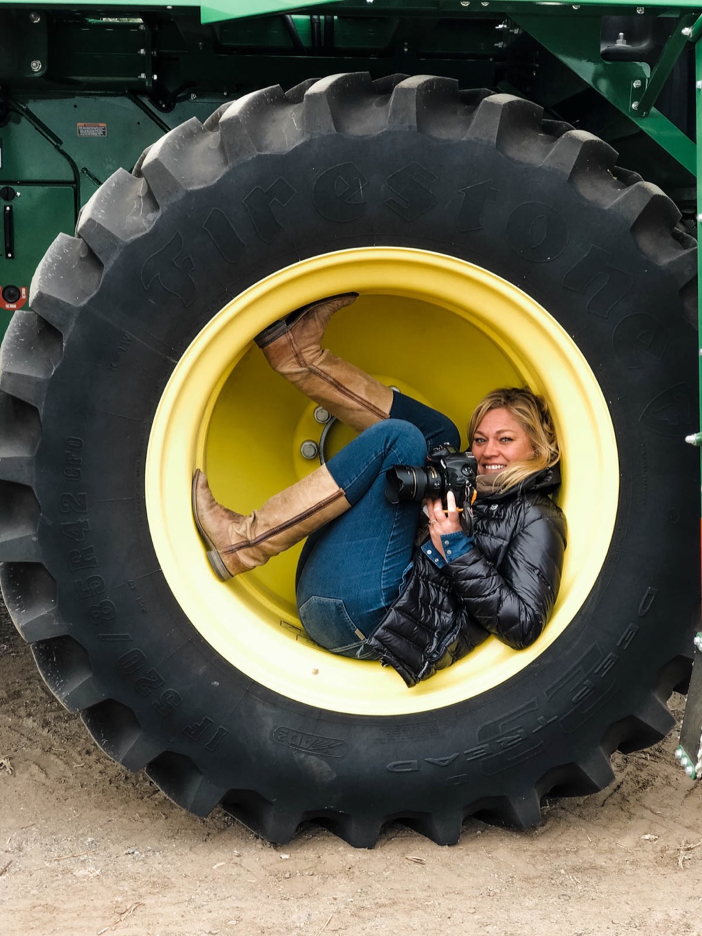 Dawn Heumann curled inside the wheel of a combine tire with her camera on an agriculture shoot