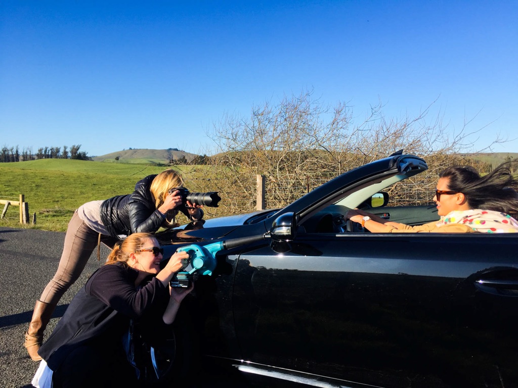 Two photographers leaning over a convertible hood to shoot the driver on a country road