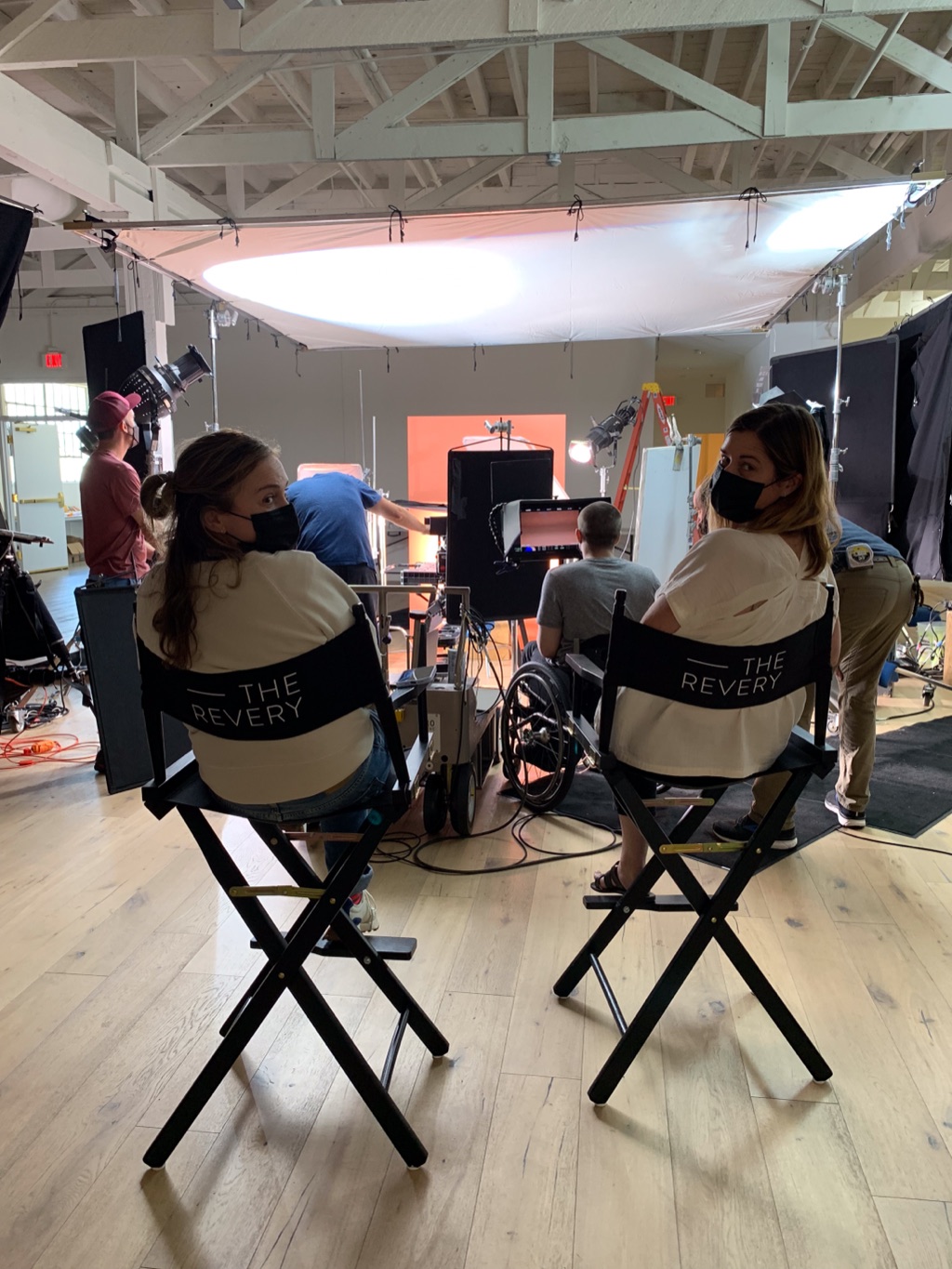 Two crew members in director's chairs turned back toward the camera while the set lights up