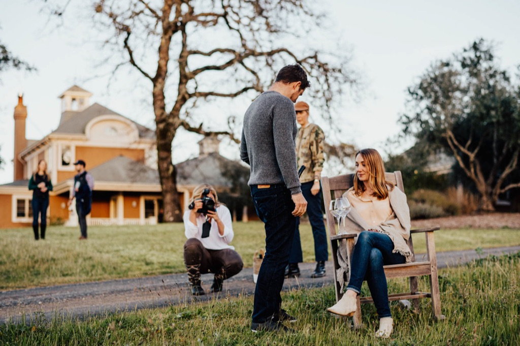 Dawn Heumann crouched on an estate lawn photographing a woman in a garden chair while crew watches