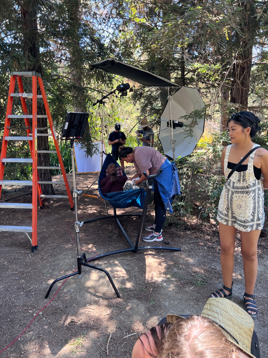 Stylist adjusting talent in a camp hammock under an octabox in the trees