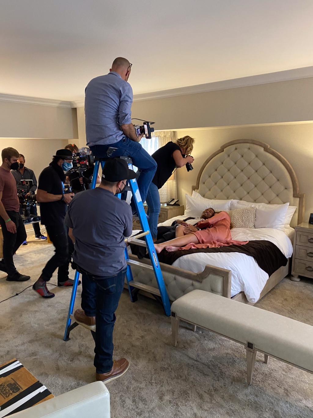 Motion crew working from ladders to film talent lying across a hotel suite bed