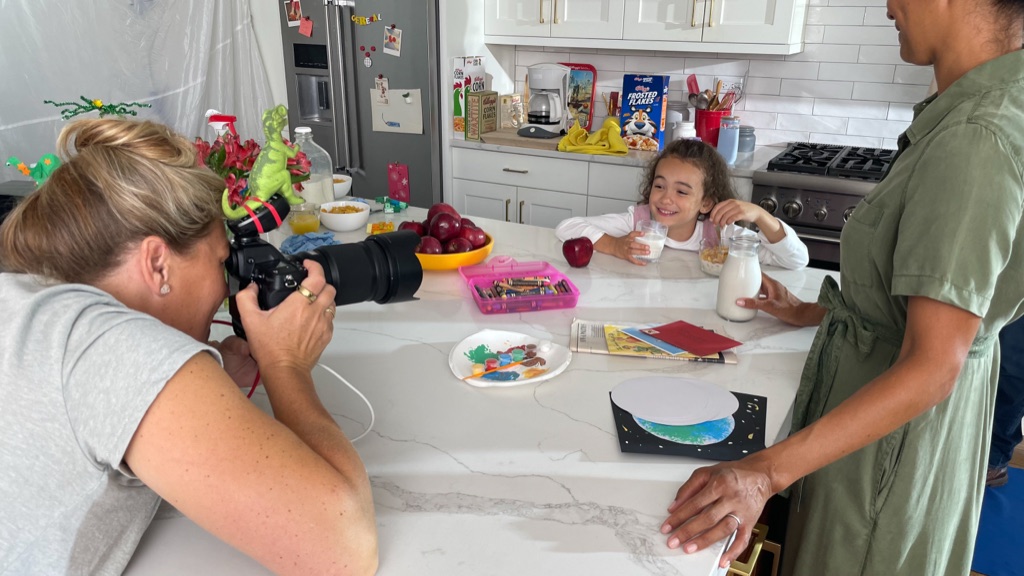 Dawn Heumann photographing a girl having cereal and milk at a kitchen counter