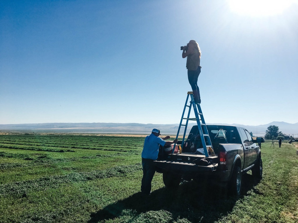 Dawn Heumann shooting from a ladder set in a pickup bed over freshly cut farm fields