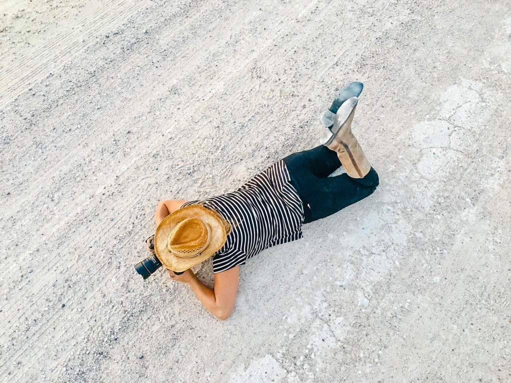 Dawn Heumann in a straw hat lying flat on a gravel road to get the low angle