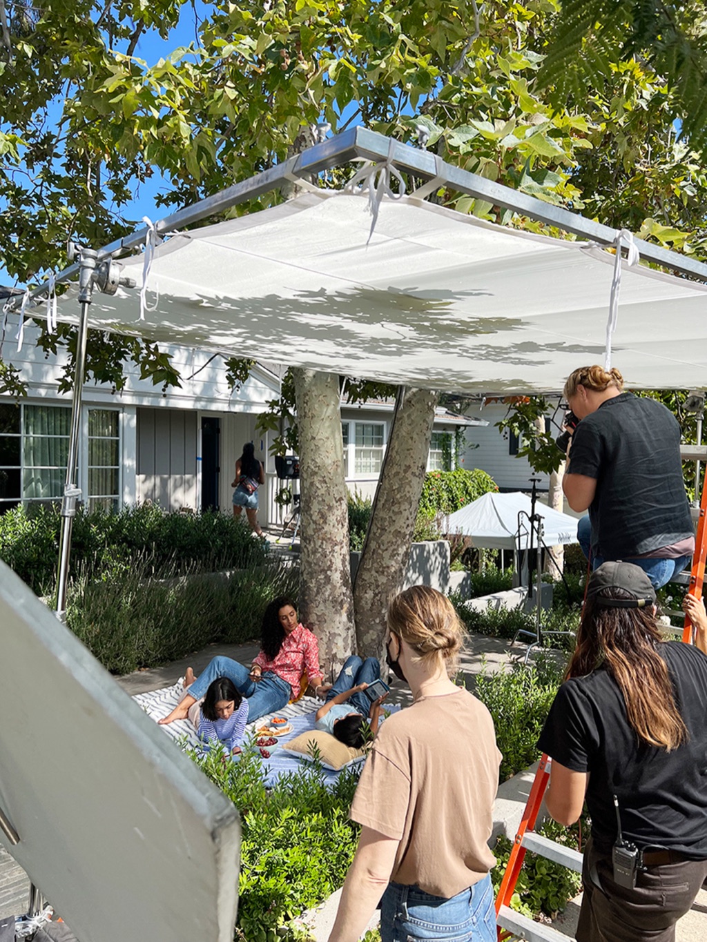 A large overhead silk rigged above a backyard picnic scene with crew working the edges