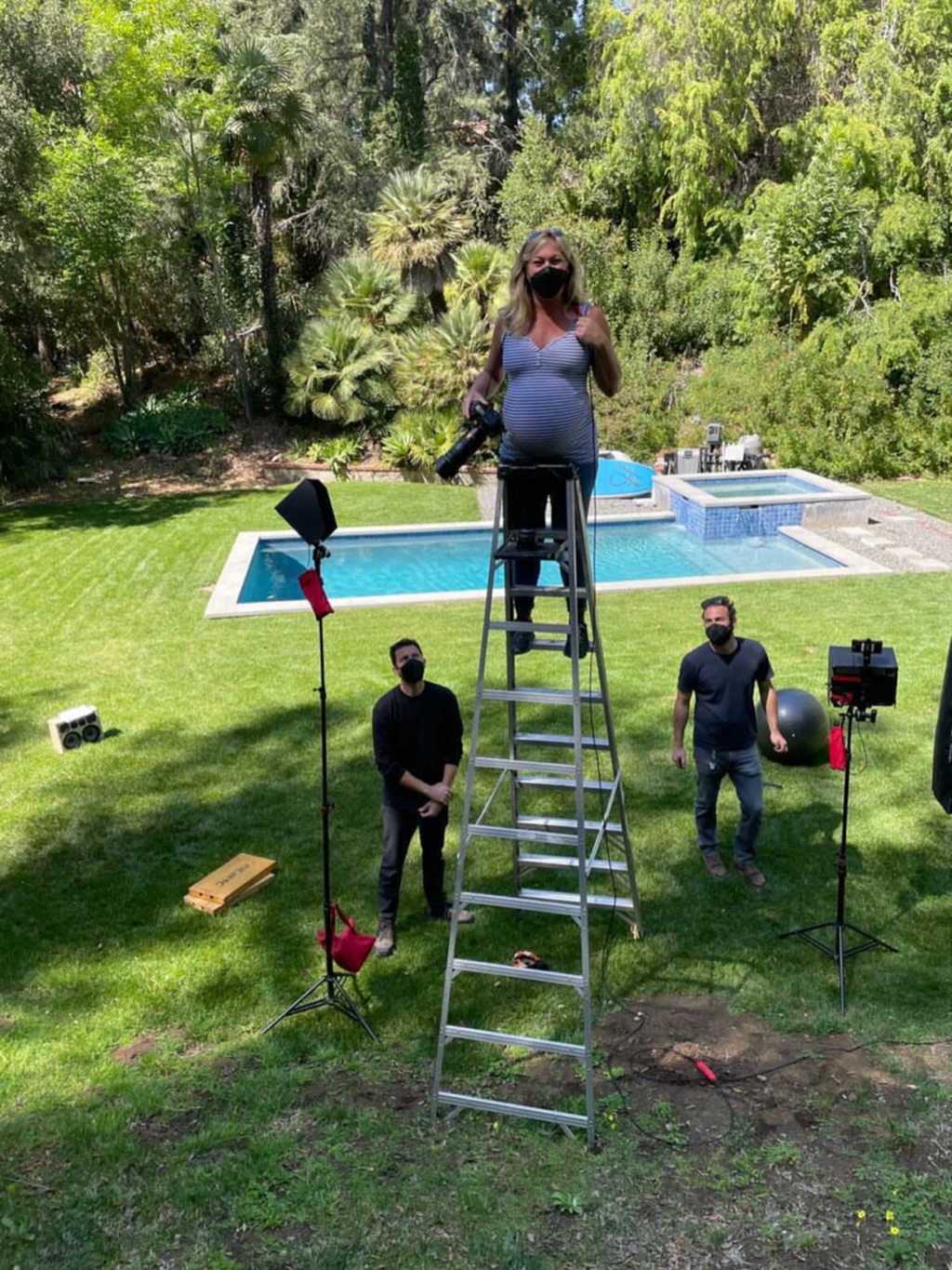 A very pregnant Dawn Heumann shooting from the top of a tall ladder over a backyard pool set