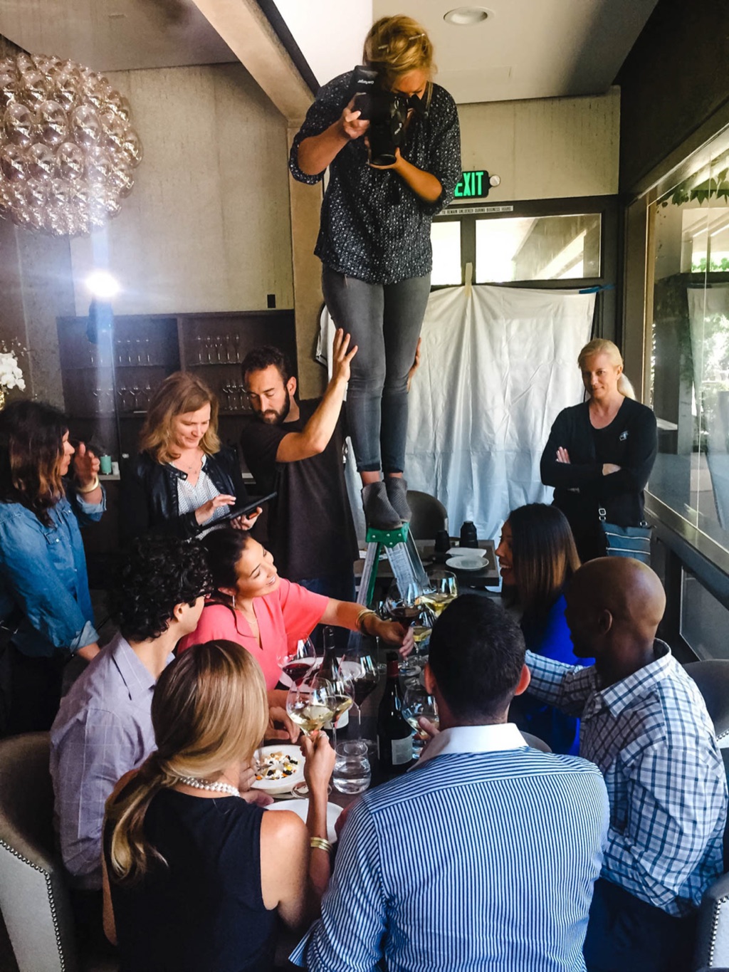 Dawn Heumann on a ladder above a styled restaurant table with crew and clients gathered around
