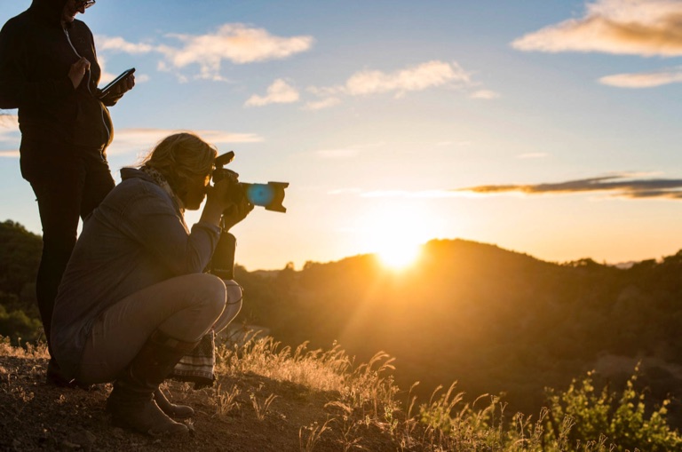 A photographer and crew shooting into the sunset from a golden hilltop ridge