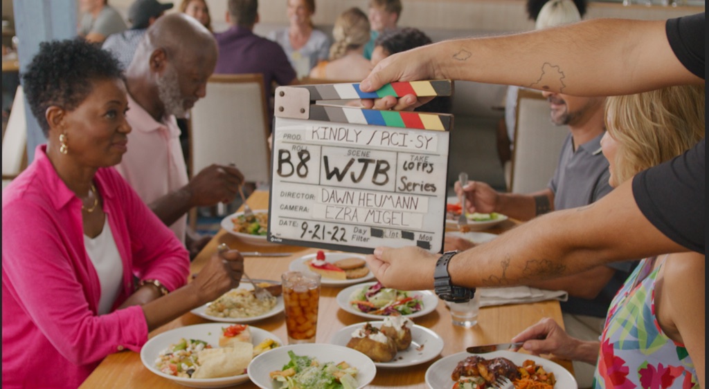 The slate drops into frame over a busy restaurant lunch scene with Dawn Heumann directing