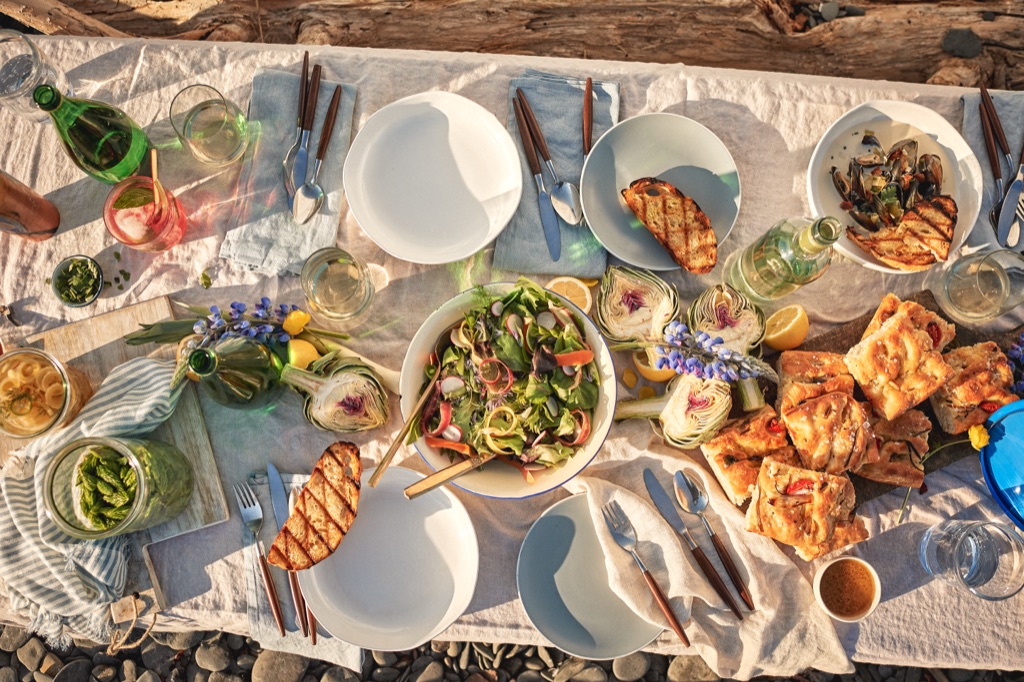 Overhead of a driftwood beach table set with mussels, focaccia, artichokes and lupine at golden hour, photographed by Dawn Heumann