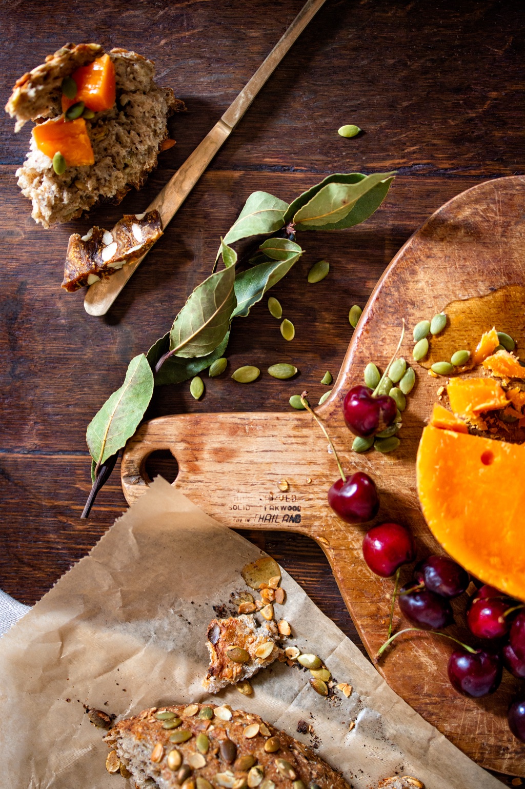 Overhead of aged cheddar, cherries, pumpkin seeds and seeded bread on a dark wood board