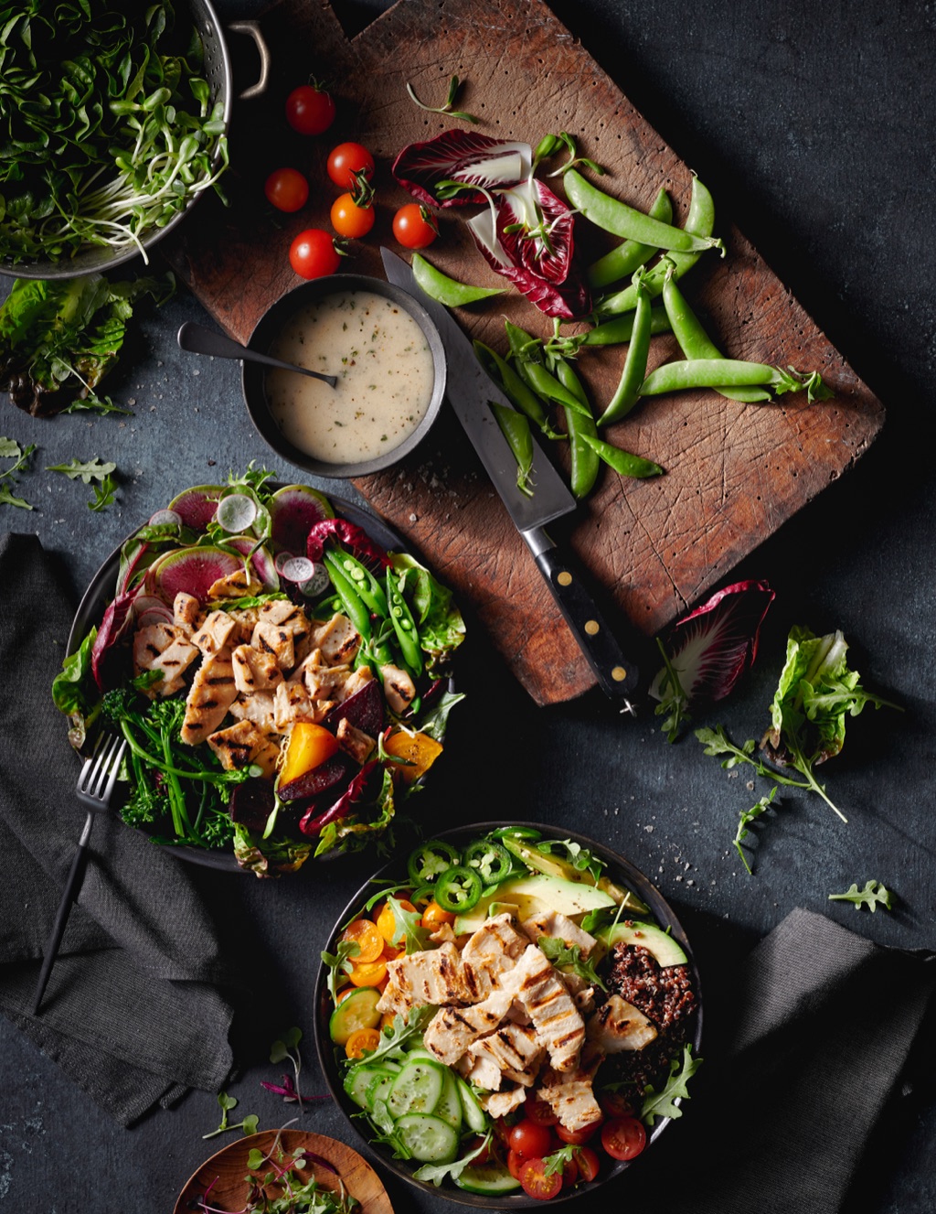 Overhead of grilled chicken salads with watermelon radish and snap peas on dark slate