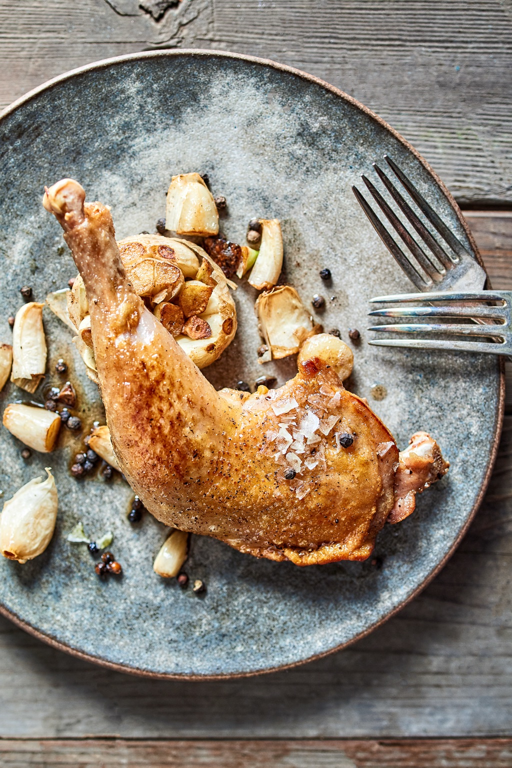Crispy chicken leg with confit garlic and peppercorns on a blue ceramic plate