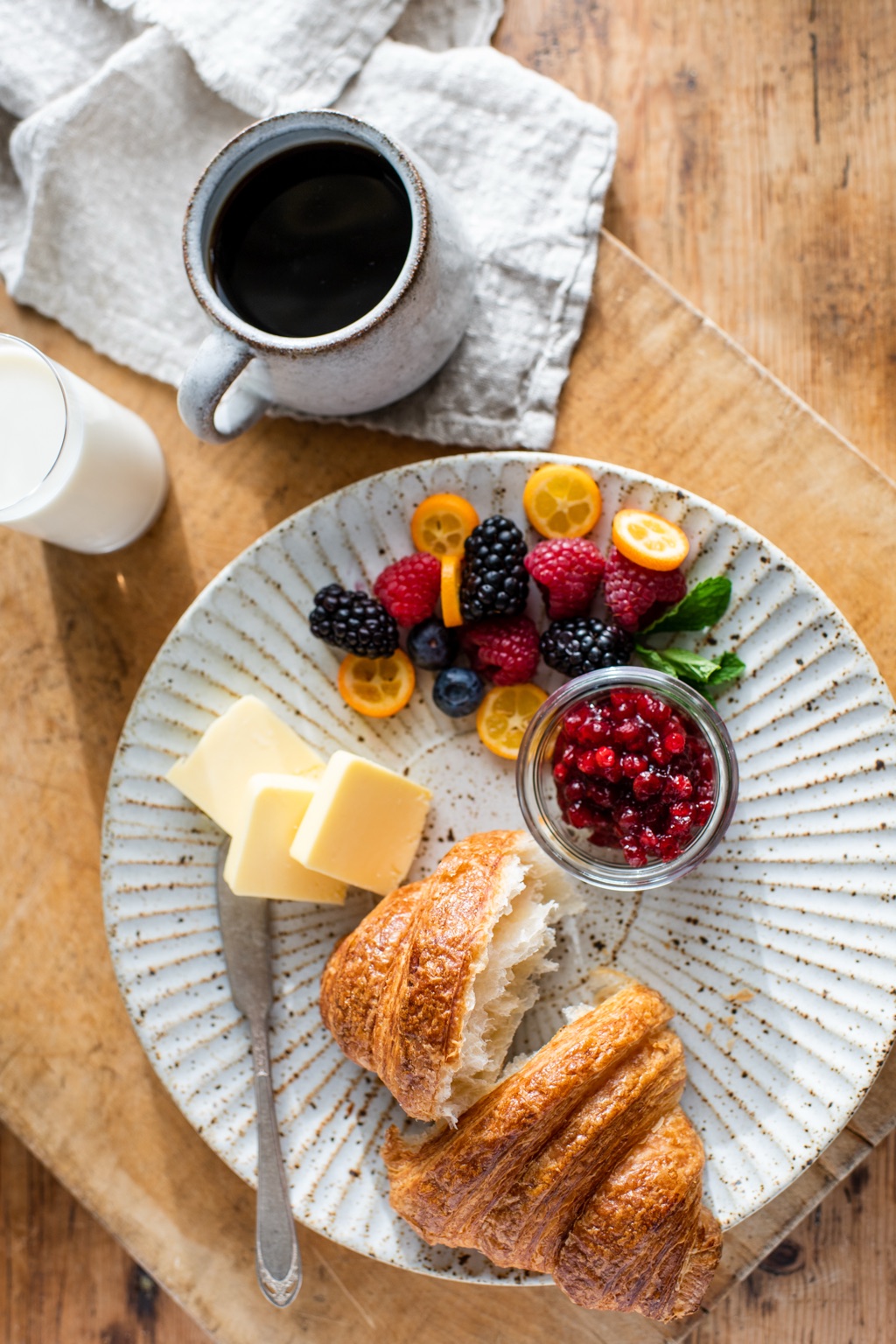 Overhead of a croissant breakfast plate with berries, kumquats, butter and lingonberry jam