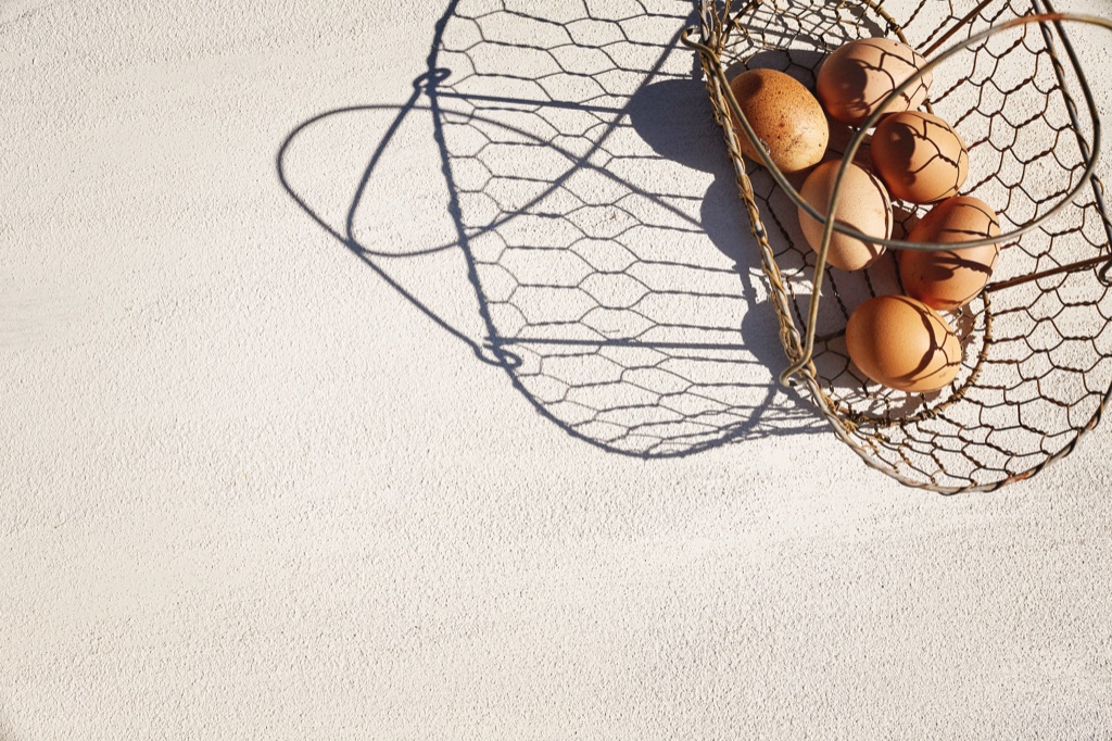 Wire basket of brown eggs casting a long shadow across sunlit plaster