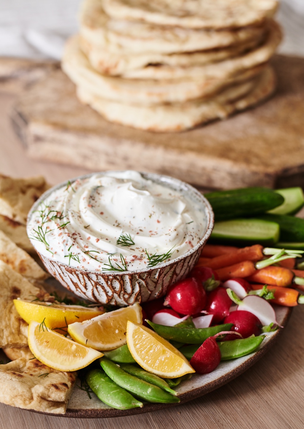 Whipped herb dip with a flatbread stack, snap peas, radishes and lemon on a wood board