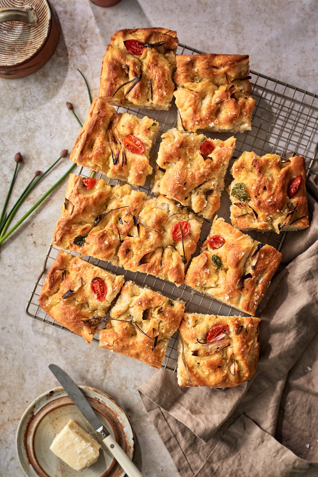 Overhead of tomato and herb focaccia squares on a wire cooling rack with butter