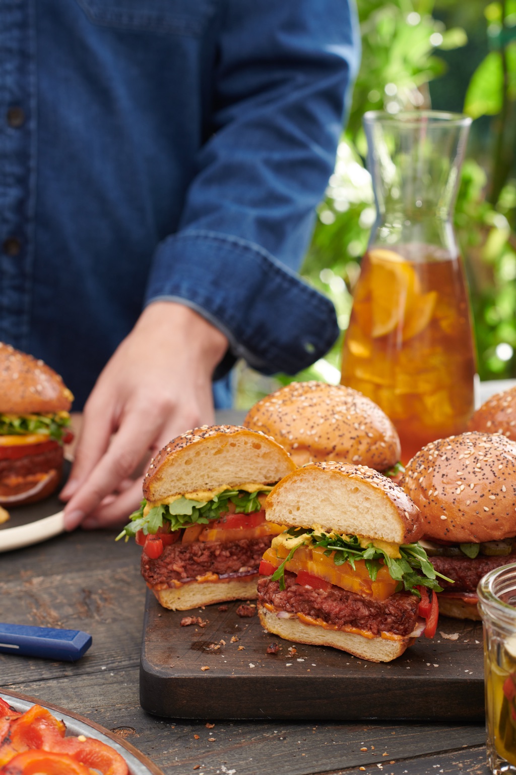 Cross-cut burgers stacked with heirloom tomato and arugula on seeded brioche at a garden table