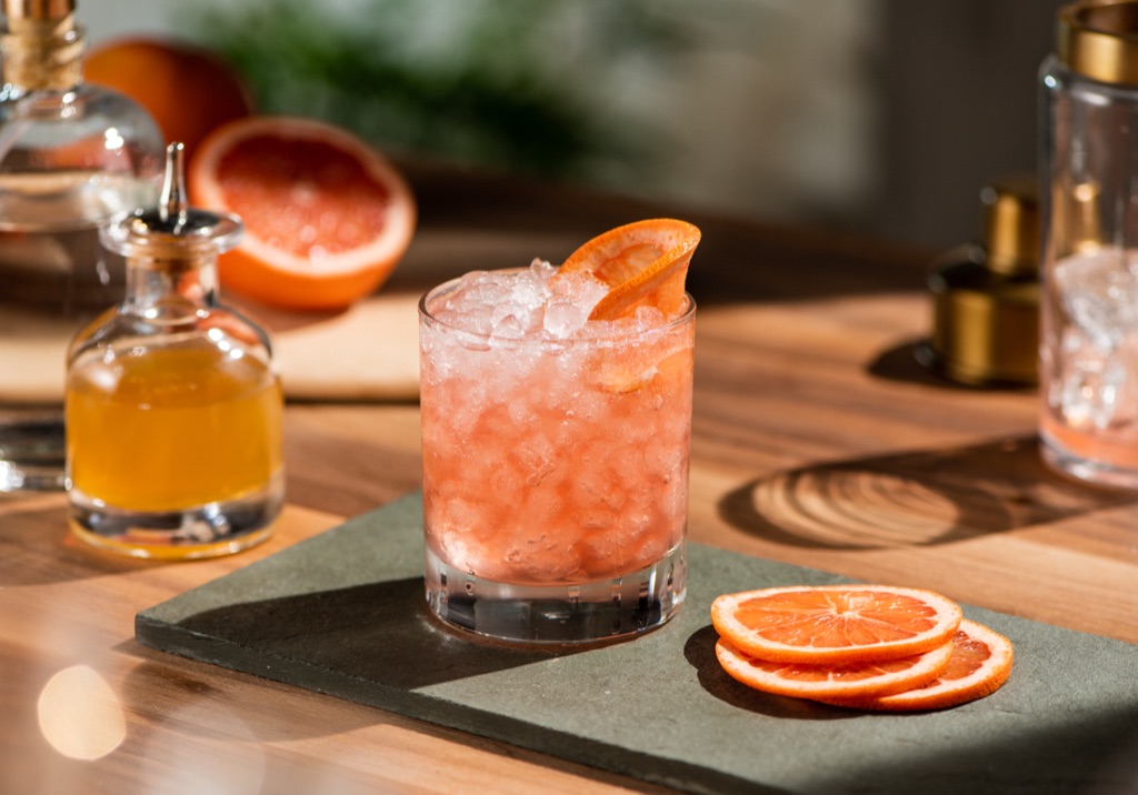 Grapefruit cocktail over crushed ice on a slate board with bitters and citrus