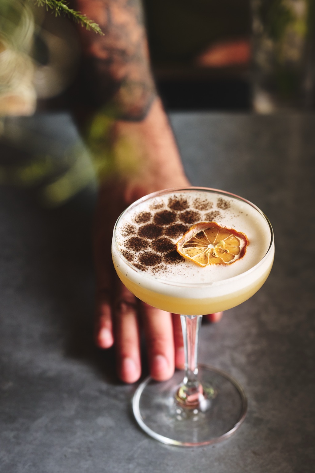 Bartender presenting a honeycomb-dusted whiskey sour with a dried lemon wheel