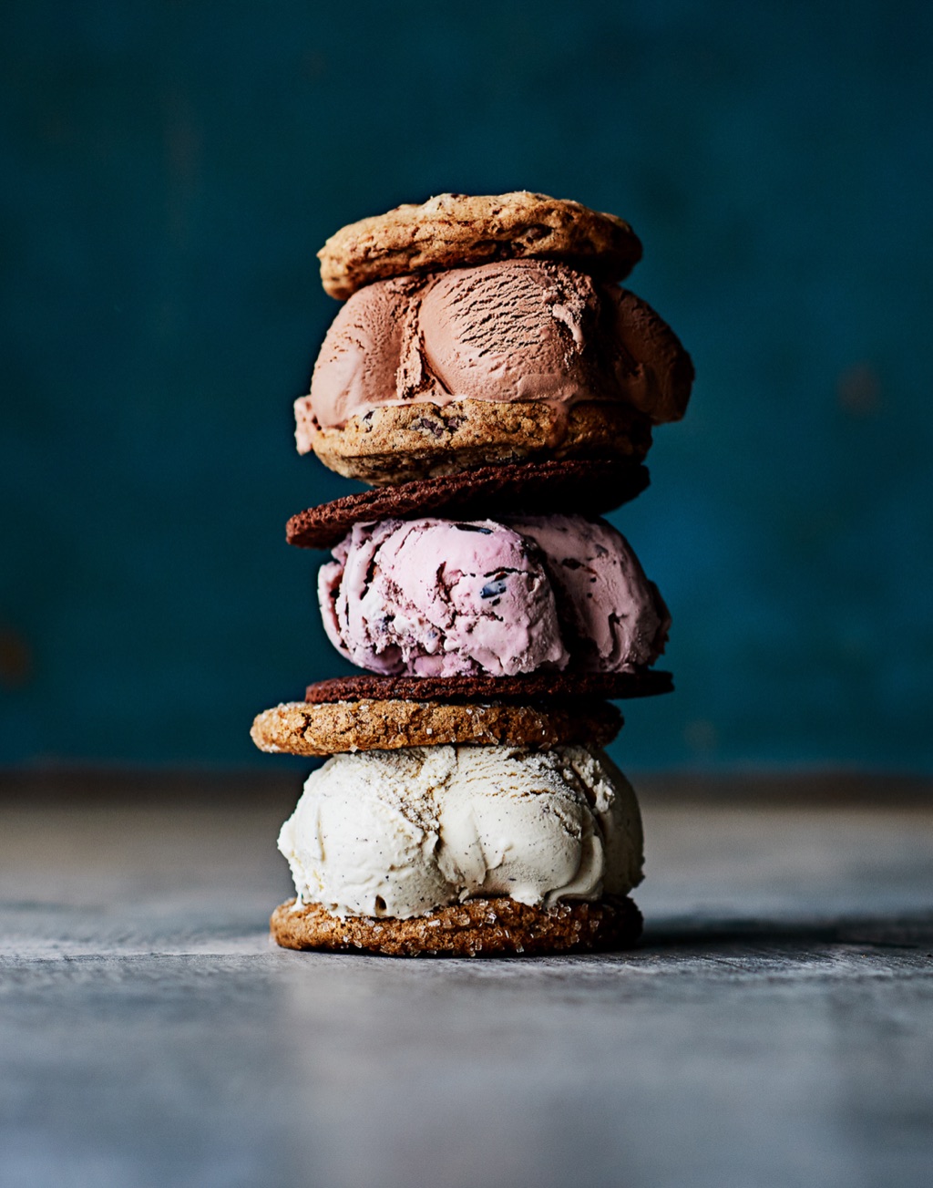 Stack of three ice cream sandwiches in chocolate, berry and vanilla against a teal wall