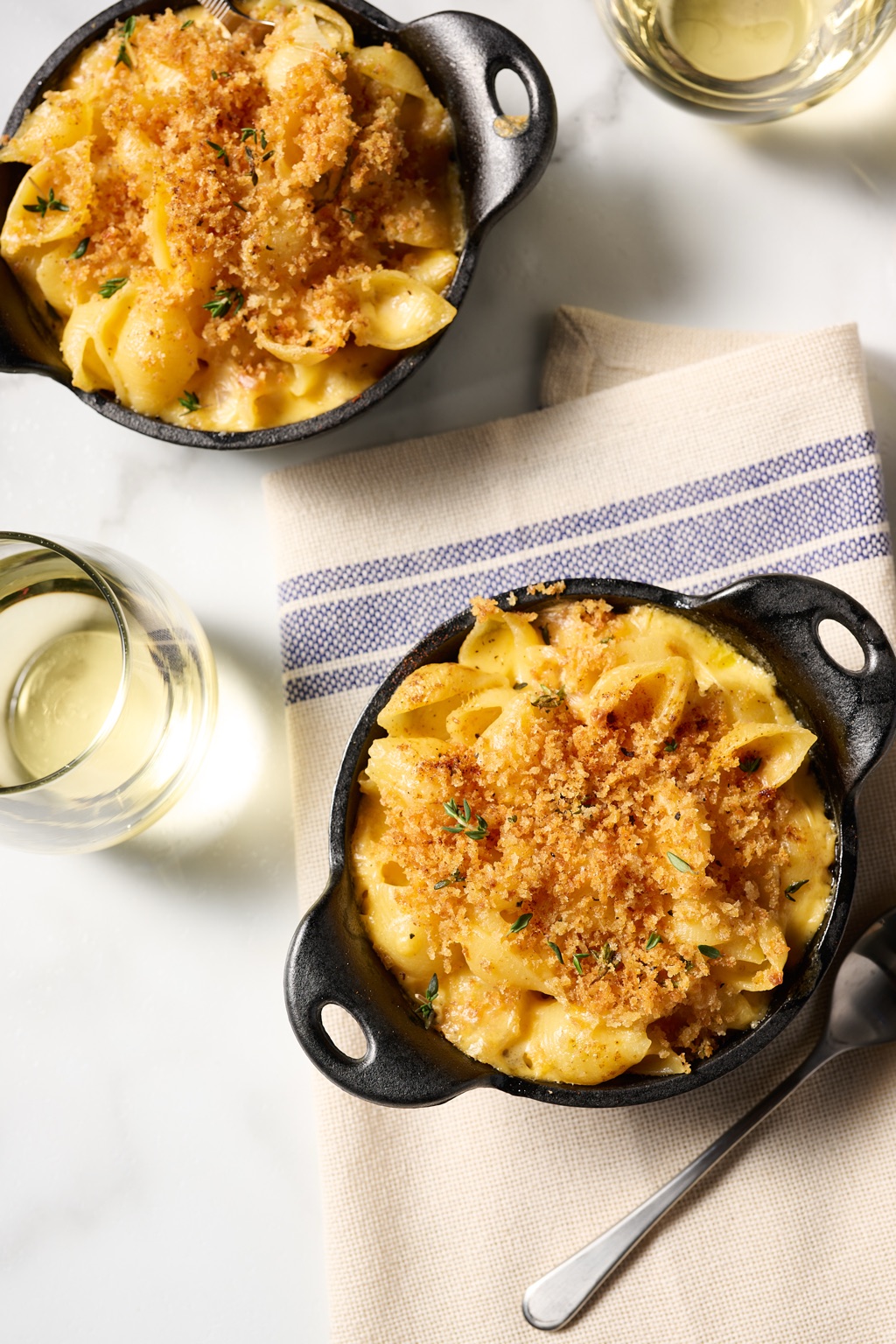 Overhead of baked mac and cheese in cast iron cocottes with thyme and glasses of white wine