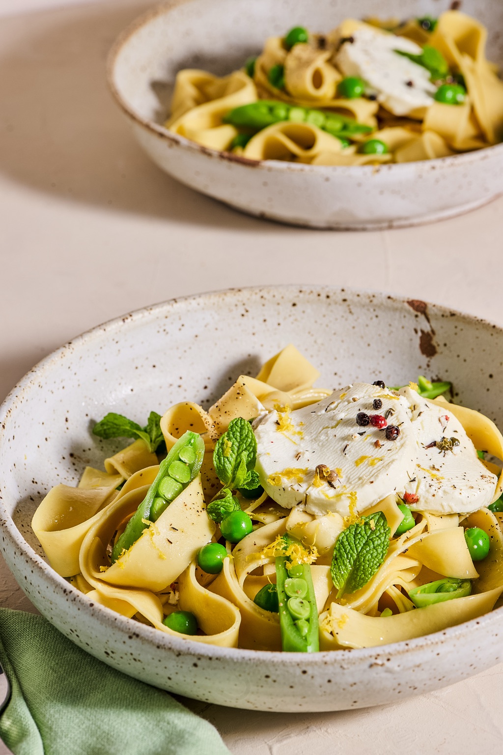 Pappardelle with spring peas, mint and a peppercorn goat cheese medallion in speckled bowls