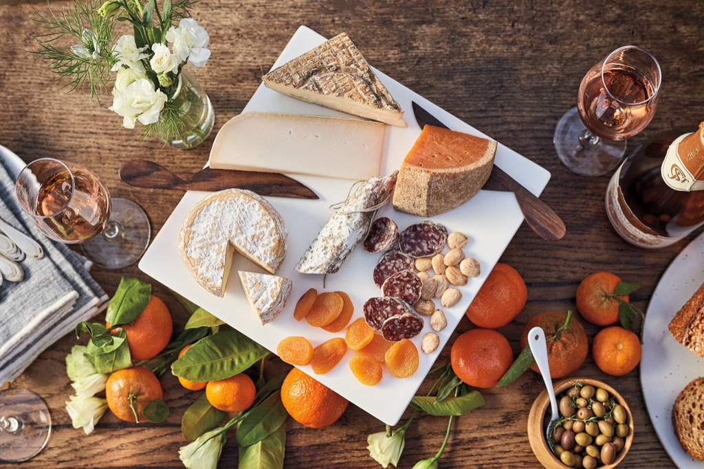 Cheese and salami board with dried apricots, mandarins and sparkling rosé in evening light