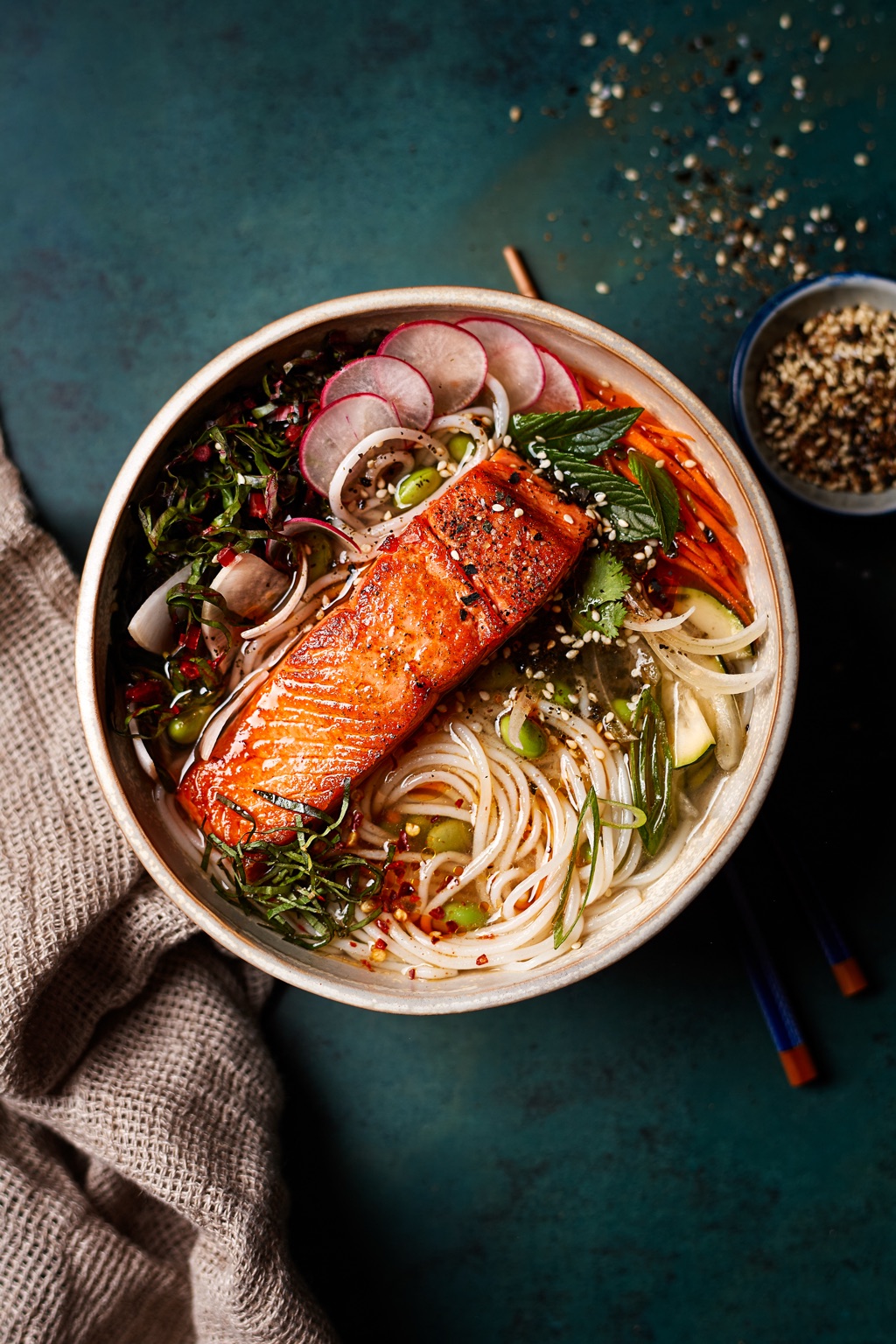 Overhead of seared salmon on rice noodles with radishes, mint and sesame