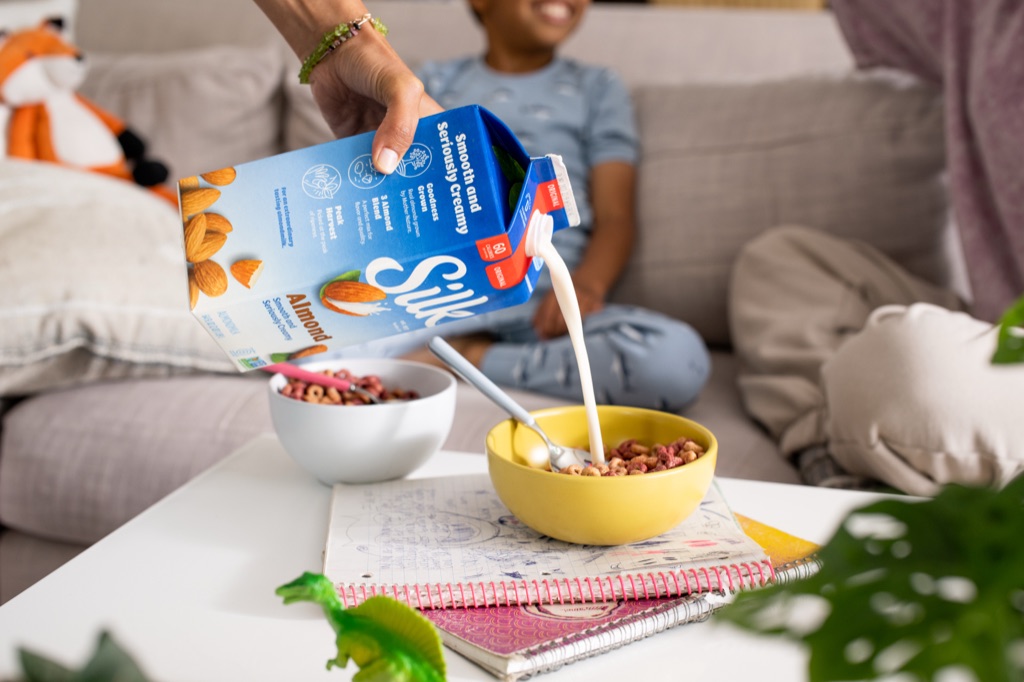 Silk almondmilk poured into a cereal bowl on a coffee table while a boy laughs on the couch