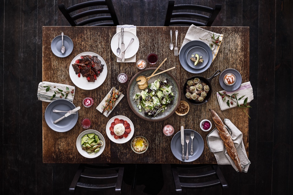 Overhead of a moody supper club table with escargot, ribs, salad and a baguette