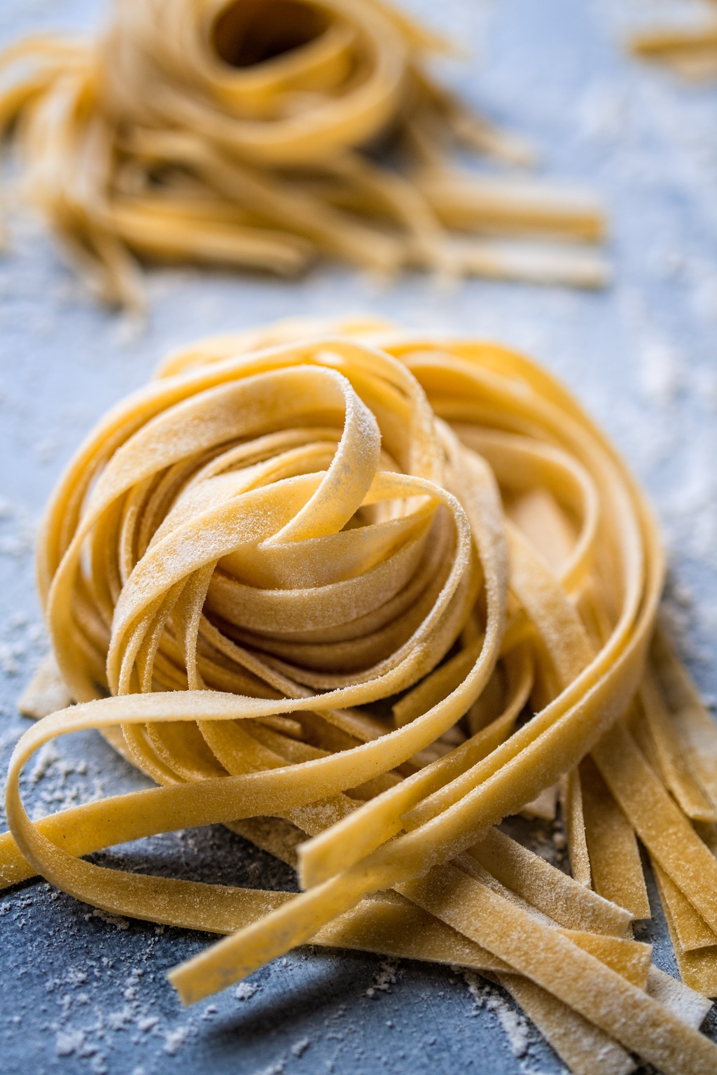 Fresh-cut tagliatelle nests dusted with flour on a blue work surface
