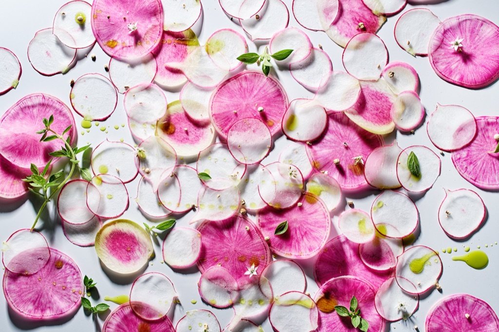 Hard-light flatlay of shaved watermelon radishes with oregano blossoms and olive oil