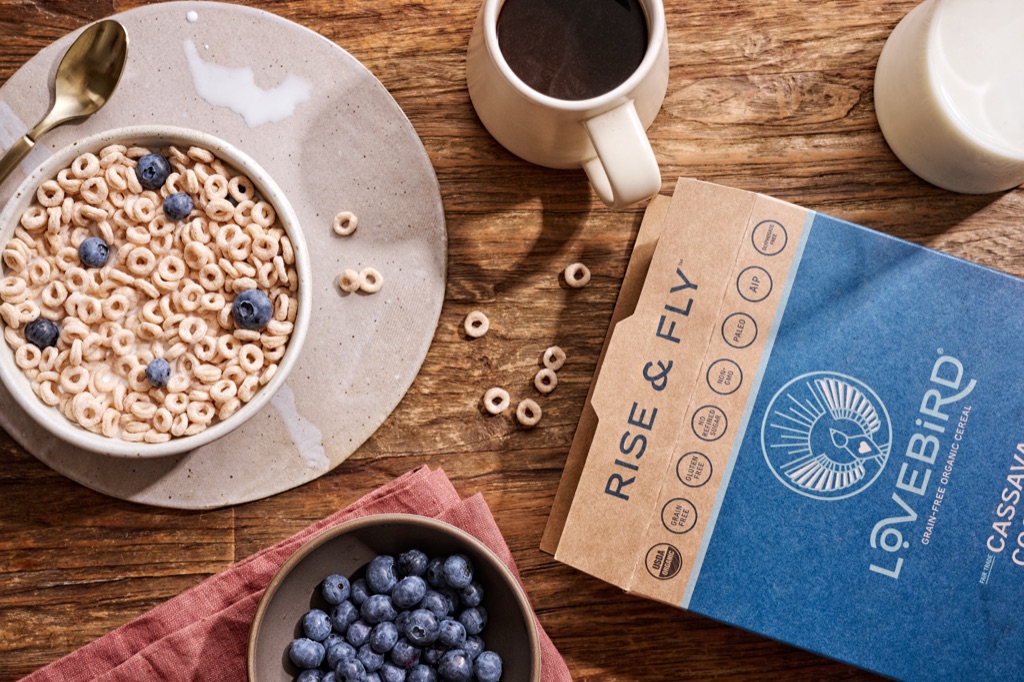Overhead breakfast of Lovebird grain free cereal with blueberries, coffee, and milk on a wood table