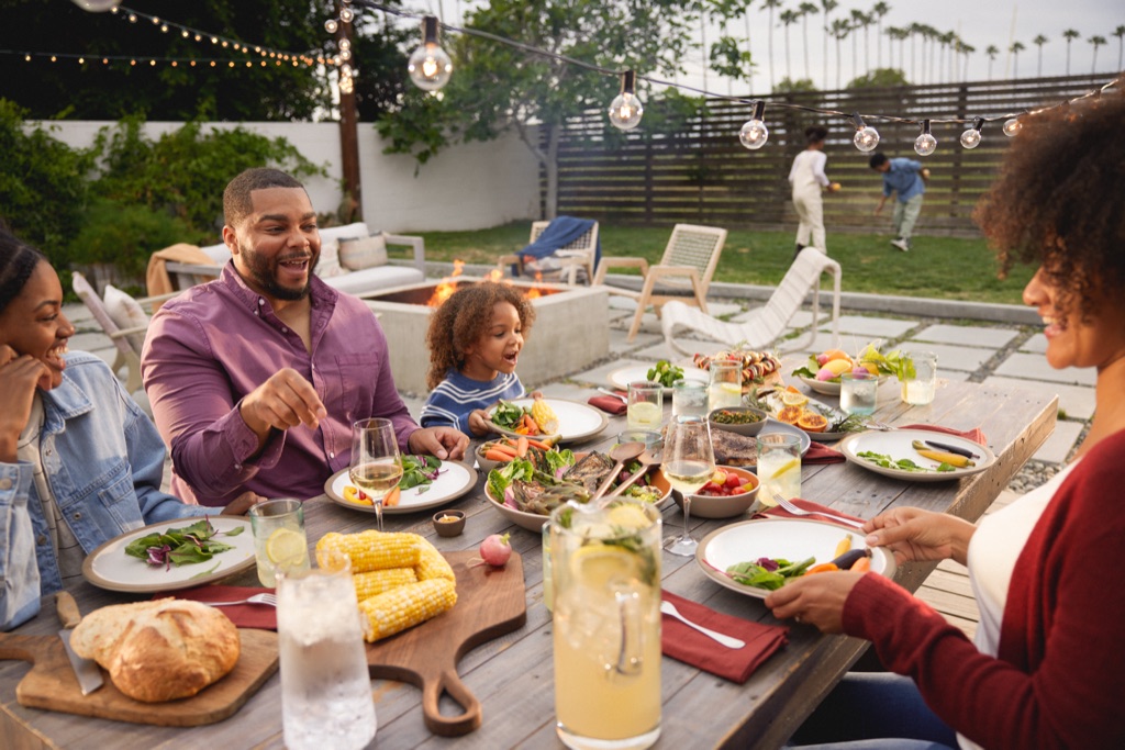 A family gathered around an outdoor dinner table at golden hour with string lights, photographed by Dawn Heumann