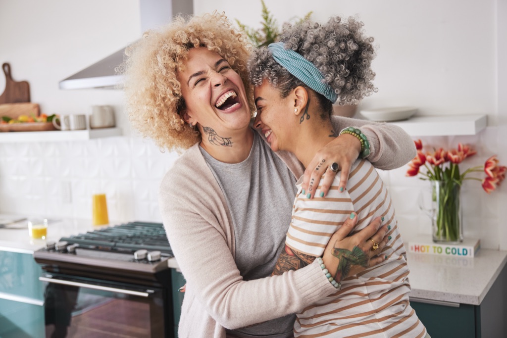 Two women laughing in a warm embrace in the kitchen with tulips on the counter