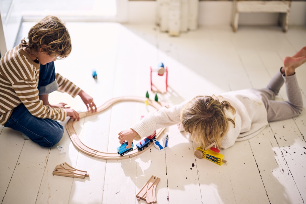 Two kids building a wooden train track on a whitewashed plank floor