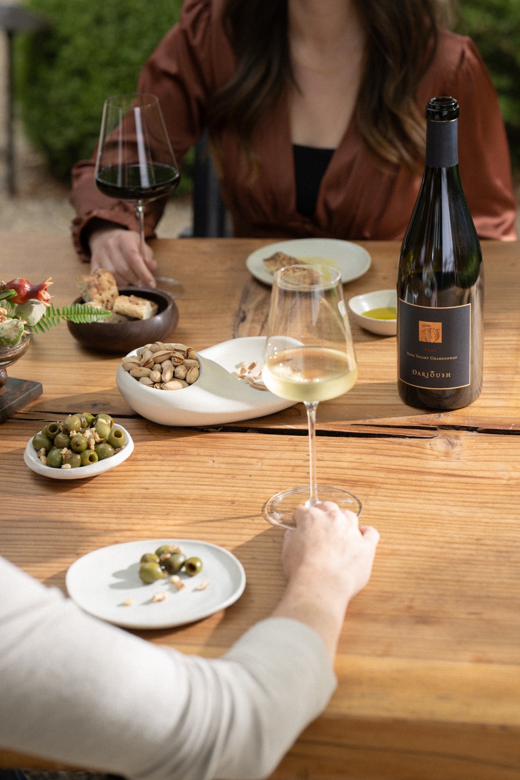Bottle of Darioush Napa Valley Chardonnay on an outdoor tasting table with olives and pistachios