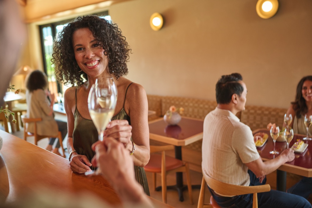 Woman smiling with a glass of sparkling wine at a warm tasting room bar