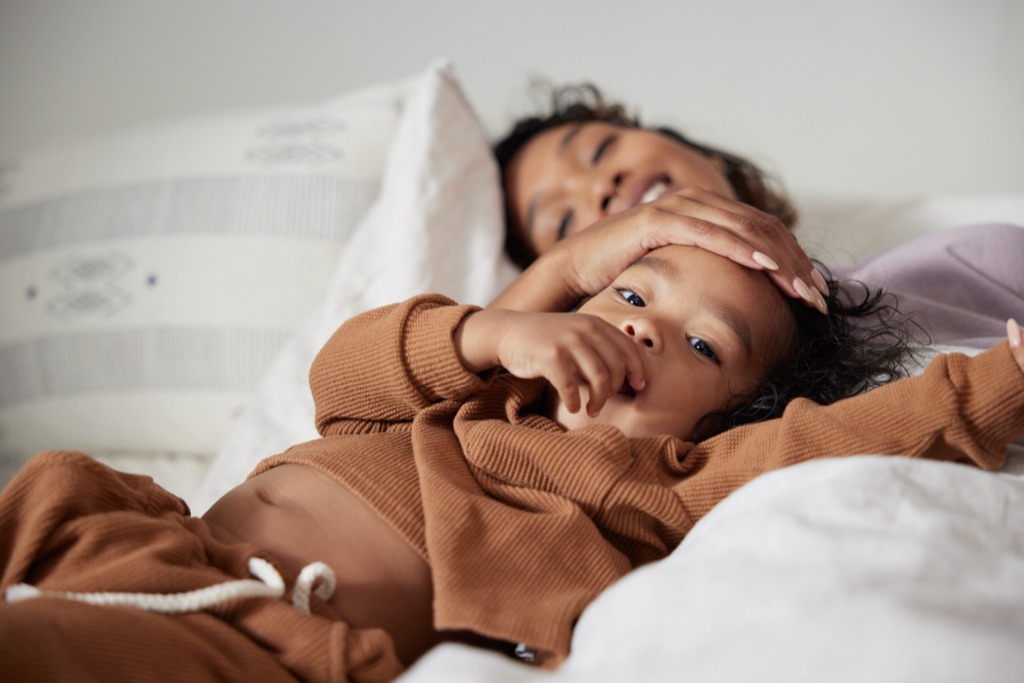 Baby in a rust waffle knit set sitting on a bed with mom's hand resting on her head