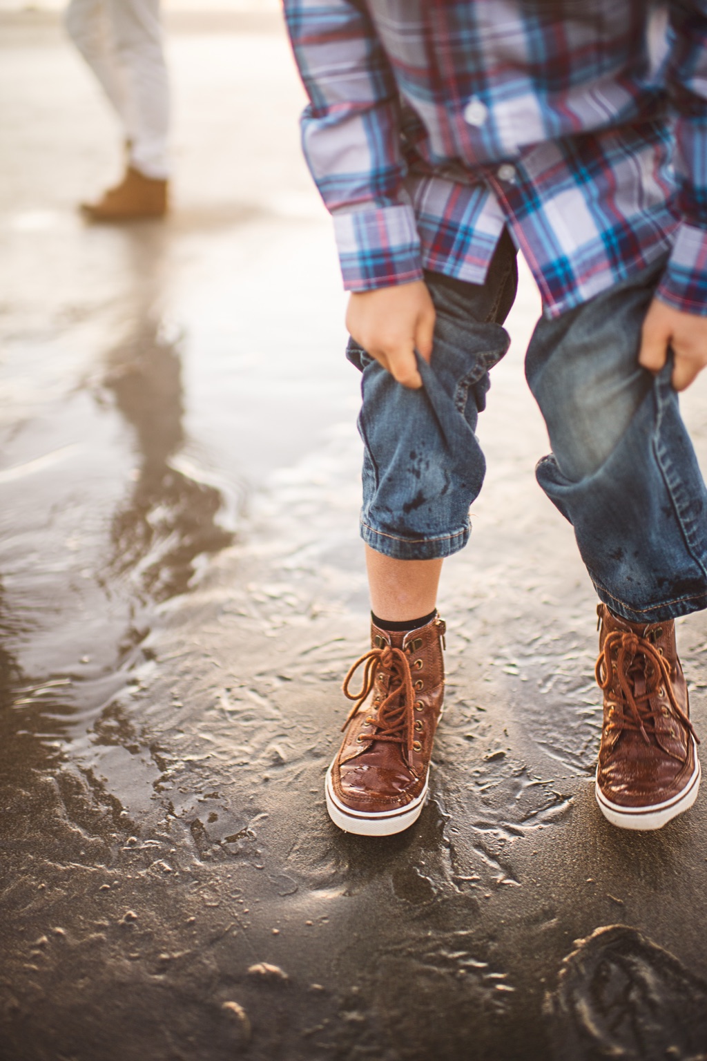 Boy rolling up his jeans cuffs on wet beach sand