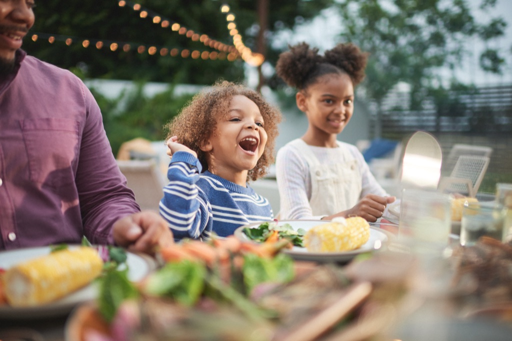 Little boy laughing at an outdoor dinner table under string lights with corn on his plate