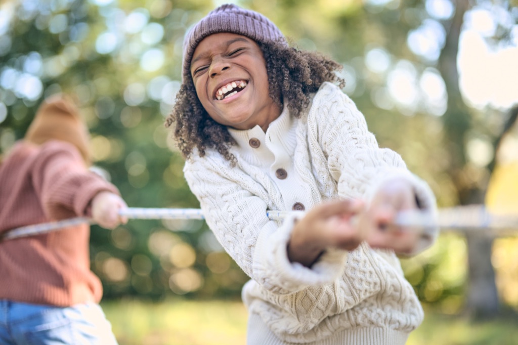 Boy in a beanie and cable knit sweater laughing while pulling a tug of war rope