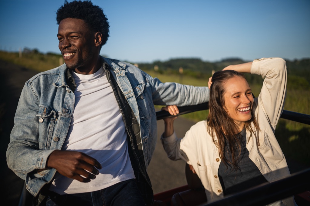 Couple laughing in the back of an open vehicle on a country road at golden hour